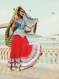 Woman in traditional clothing standing by railing against sky