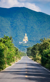 Road amidst plants against buddha statue in sunny day