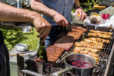Close-up of man holding utensil and grilling meat in back yard.