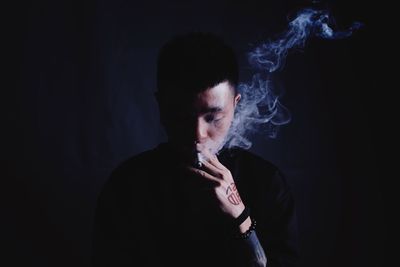 Close-up of man smoking cigarette against black background