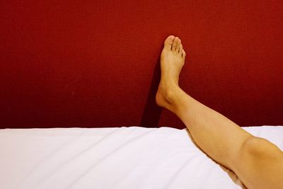 Low section of woman lying on bed by red wall