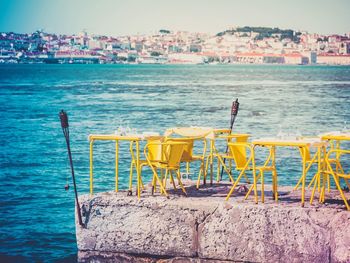 Chairs and table by sea against buildings in city