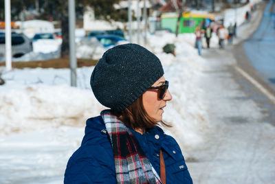 Mature woman looking away on snow covered footpath during winter