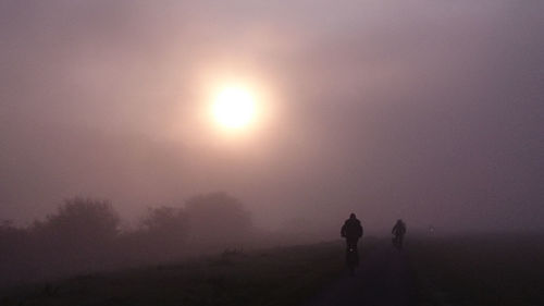 Silhouette people on field against sky during sunset