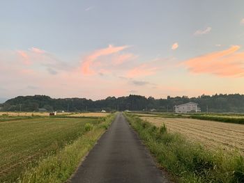 Empty road amidst field against sky during sunset