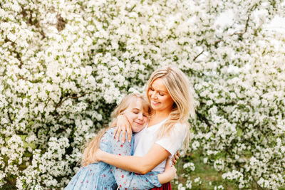 View of mother and daughter embracing against flowering plant outdoors