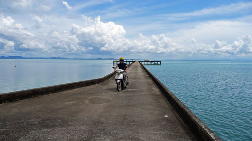 Man riding motorcycle on pier over sea