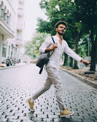 Full length of young man carrying backpack while walking on cobbled street in city