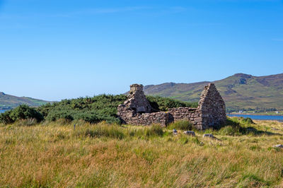 Stone wall on field against clear blue sky