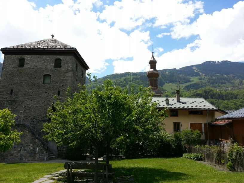 building exterior, architecture, built structure, sky, religion, church, place of worship, spirituality, cloud - sky, tree, cross, cloud, grass, mountain, green color, tower, day, outdoors