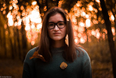 Portrait of young woman standing against illuminated tree