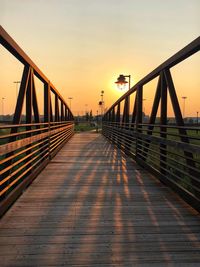 Footbridge over footpath against sky during sunset