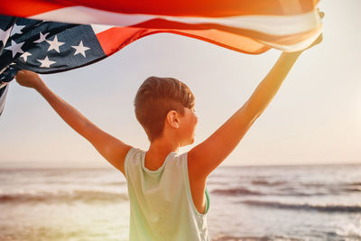 Rear view of man holding flag at beach against sky