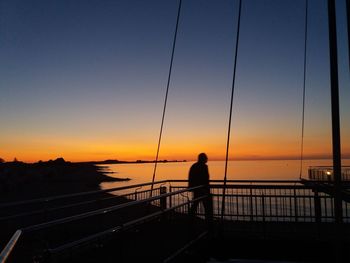 Silhouette woman standing on bridge against sea during sunset