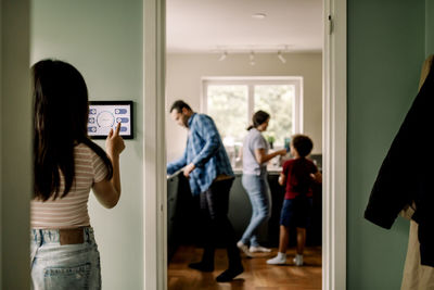 Rear view of girl using home automation on wall by doorway