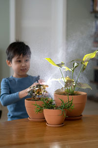 A boy sprays flowers in orange clay terracotta pots with a spray gun.