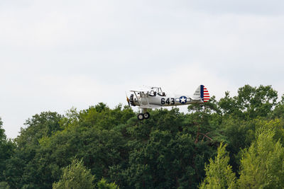 Airplane flying by trees against sky