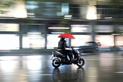 Blurred motion of man with umbrella riding motorcycle on street at night