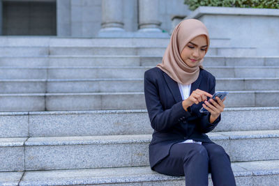 Full length of man using mobile phone while sitting outdoors