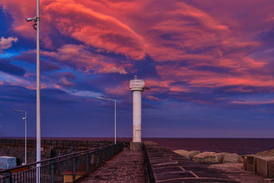 Lighthouse by sea against sky during sunset