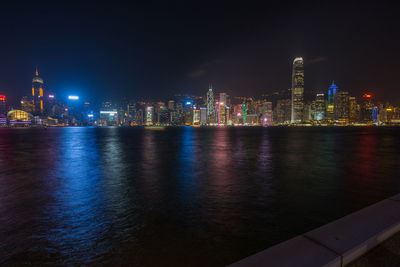 Illuminated buildings by river against sky at night