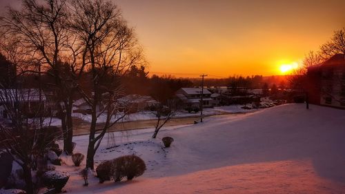 Bare trees on snow covered landscape during sunset