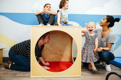 Teachers and 3 students gather next to, inside and on top of a cube