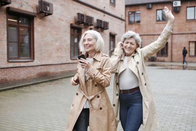 Happy young woman using mobile phone on street in city