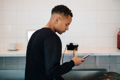 Side view of young male photographer using smart phone sitting at cafe