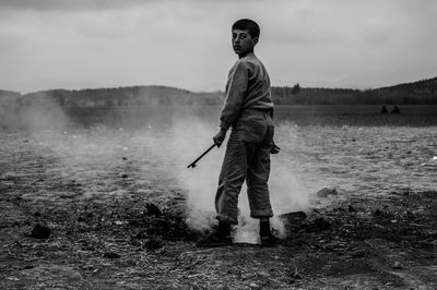 Portrait of boy standing on field against sky