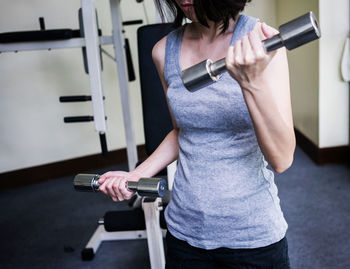 Midsection of woman exercising with dumbbells at gym