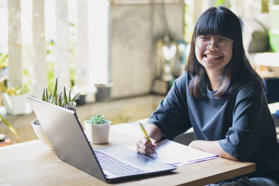 Portrait of young woman using phone while sitting on table