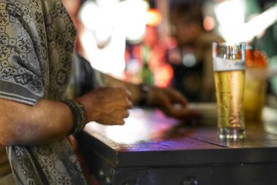 Midsection of person holding beer glass on table