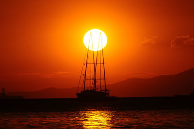 Silhouette sailboat on sea against orange sky