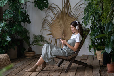 Happy girl florist in indoor garden listen music buy houseplant for gardening with smartphone online