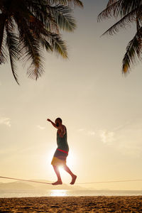 Man slacklining on rope at beach against sky during sunset