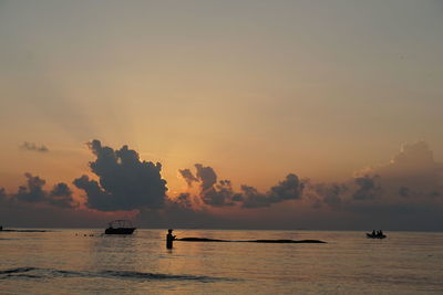 Silhouette people in sea against sky during sunset