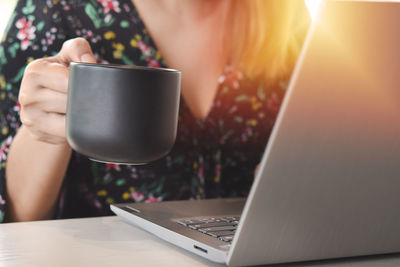 Midsection of woman holding coffee cup on table