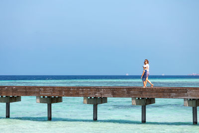 Mother and son crossing a wooden bridge looking the ocean