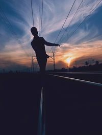 Silhouette man standing on street against sky during sunset