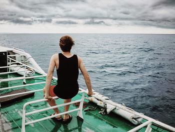 Rear view of man on boat at sea against cloudy sky