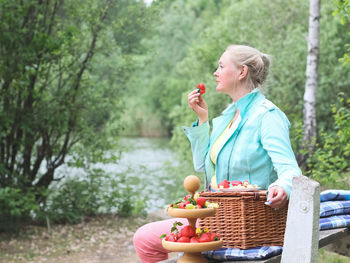 Portrait of a beautiful middle-aged caucasian blonde woman eating a big red and ripe strawberry