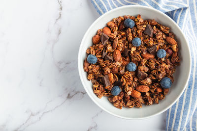 Homemade chocolate granola with almonds, hazelnuts and blueberries on white marble background.