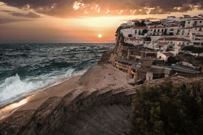 Buildings by sea against cloudy sky at sunset