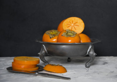 Still life with persimmon on a gray cement background in a pewter dish,