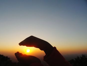 Silhouette hand holding sun against sky during sunset