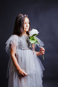 Girl holding white flower while standing against black wall
