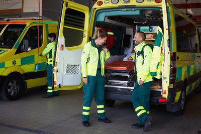 Smiling male paramedic looking at female coworker talking on walkie-talkie while standing by ambulance in parking lot