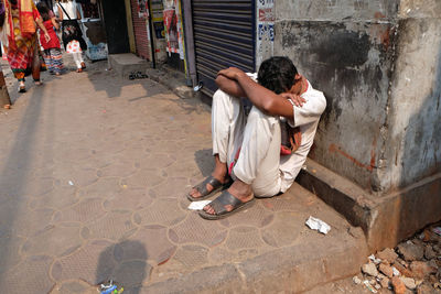Full length of boy sitting on street against building in city