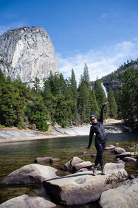 Full length of woman standing on rock at river against sky